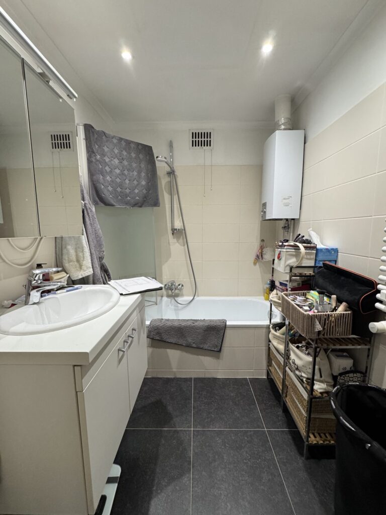 Salle de bain avant rénovation à Bruxelles : baignoire, chauffe-eau apparent, carrelage d'origine